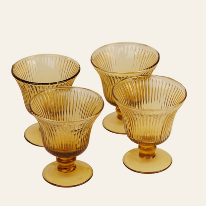 Set of four amber glass goblets with ribbed design on a white background