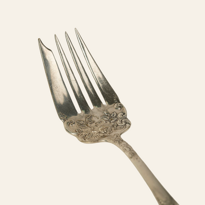 A silver-plated serving fork with floral patterns on the handle.