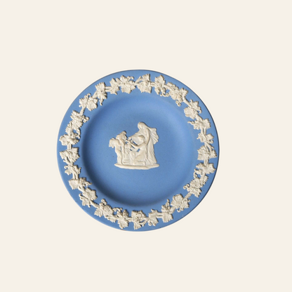 Blue decorative plate with white floral design and central figure on a white background