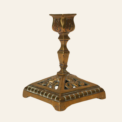 An antique brass candle stand with a carved ornate base and a simple, elongated holder on top.