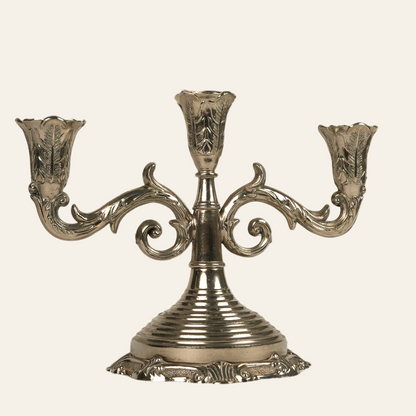 Antique three-arm silver-plated candelabra with ornate detailing and a ribbed central stem, resting on an intricately cast base.