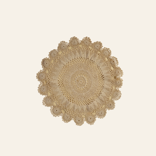 A round beige crocheted lace doily with a scalloped edge, displayed flat against a solid cream background.