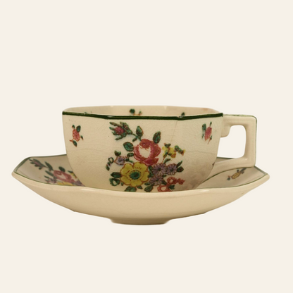 A vintage Royal Doulton ceramic cup and saucer with floral patterns and green trim.