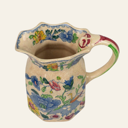 A small ceramic jug with a floral pattern featuring blues, reds, and yellows, indicative of a vintage design.