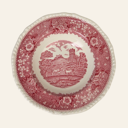 A vintage stew bowl featuring a red and white pastoral design with cows, trees, and a wooden bridge, surrounded by a floral border.