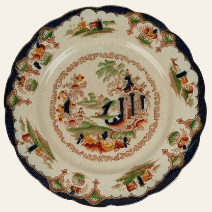 Antique ceramic plate with a central oriental landscape motif surrounded by a blue border, featuring floral and animal patterns.
