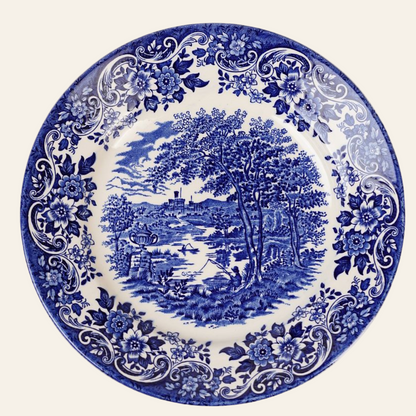 A blue luncheon plate with a floral border and a pastoral vignette in the center.