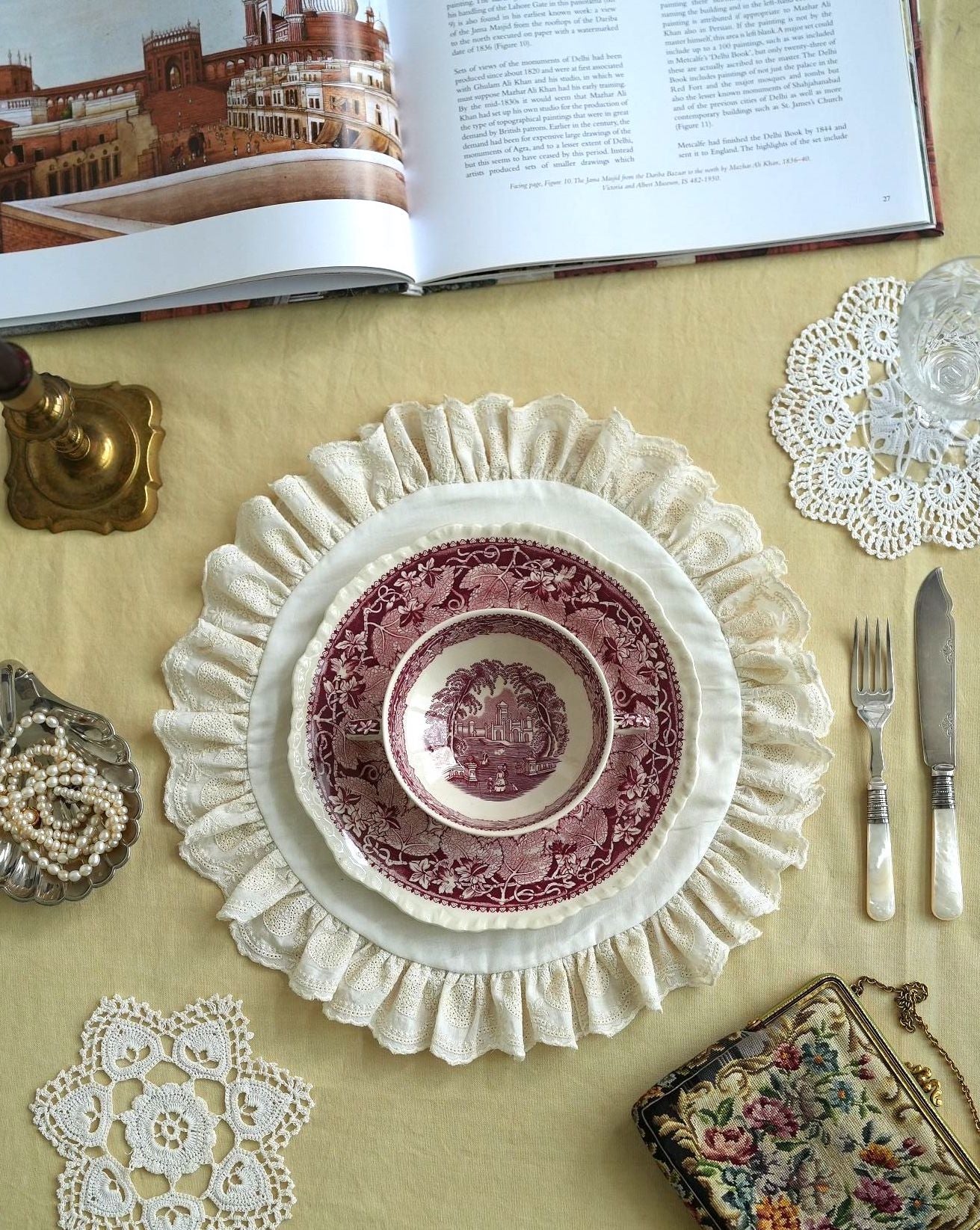 Vintage-style table setting with a pink ceramic bowl and lace doilies on a yellow surface.