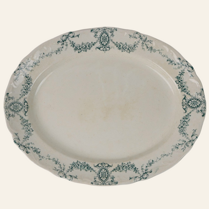An oval-shaped antique platter with a green floral pattern around the rim on a white background.
