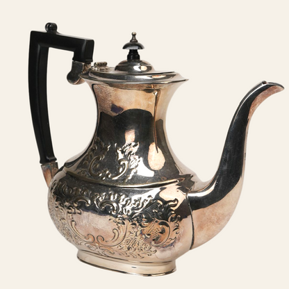 An embossed silver coffee pot with a sleek black handle and ornate detailing, showcasing a vintage style.