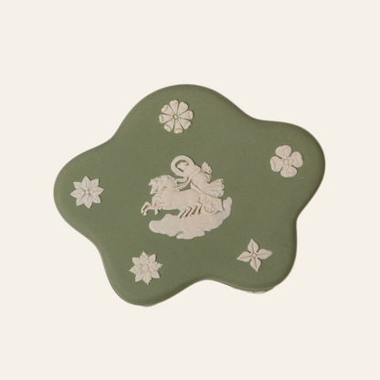 A vintage Wedgwood Jasperware trinket box in green color with a white relief of a classical figure riding a chariot, surrounded by floral motifs.