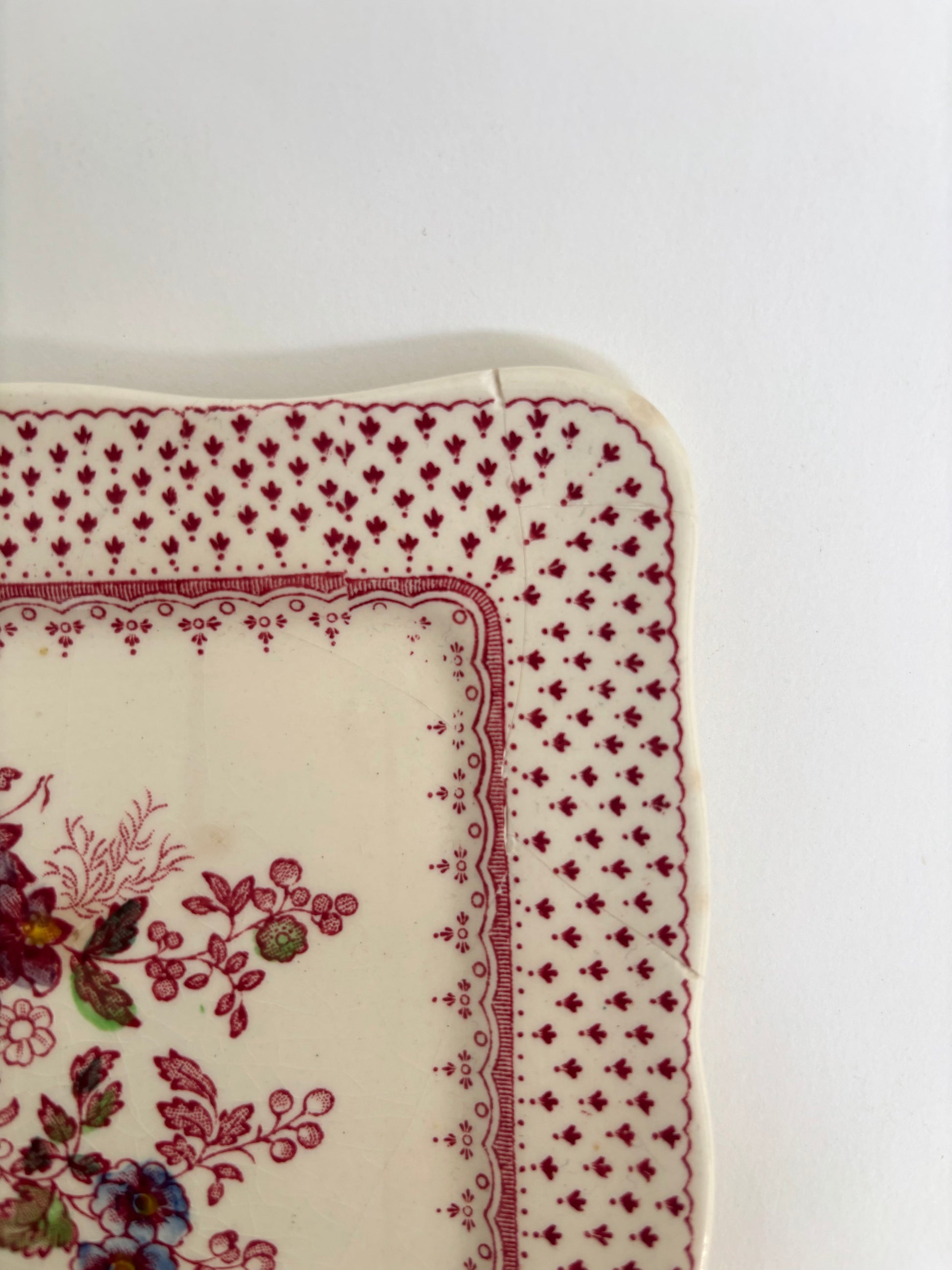 Corner of a floral-patterned fabric with red border on a white background