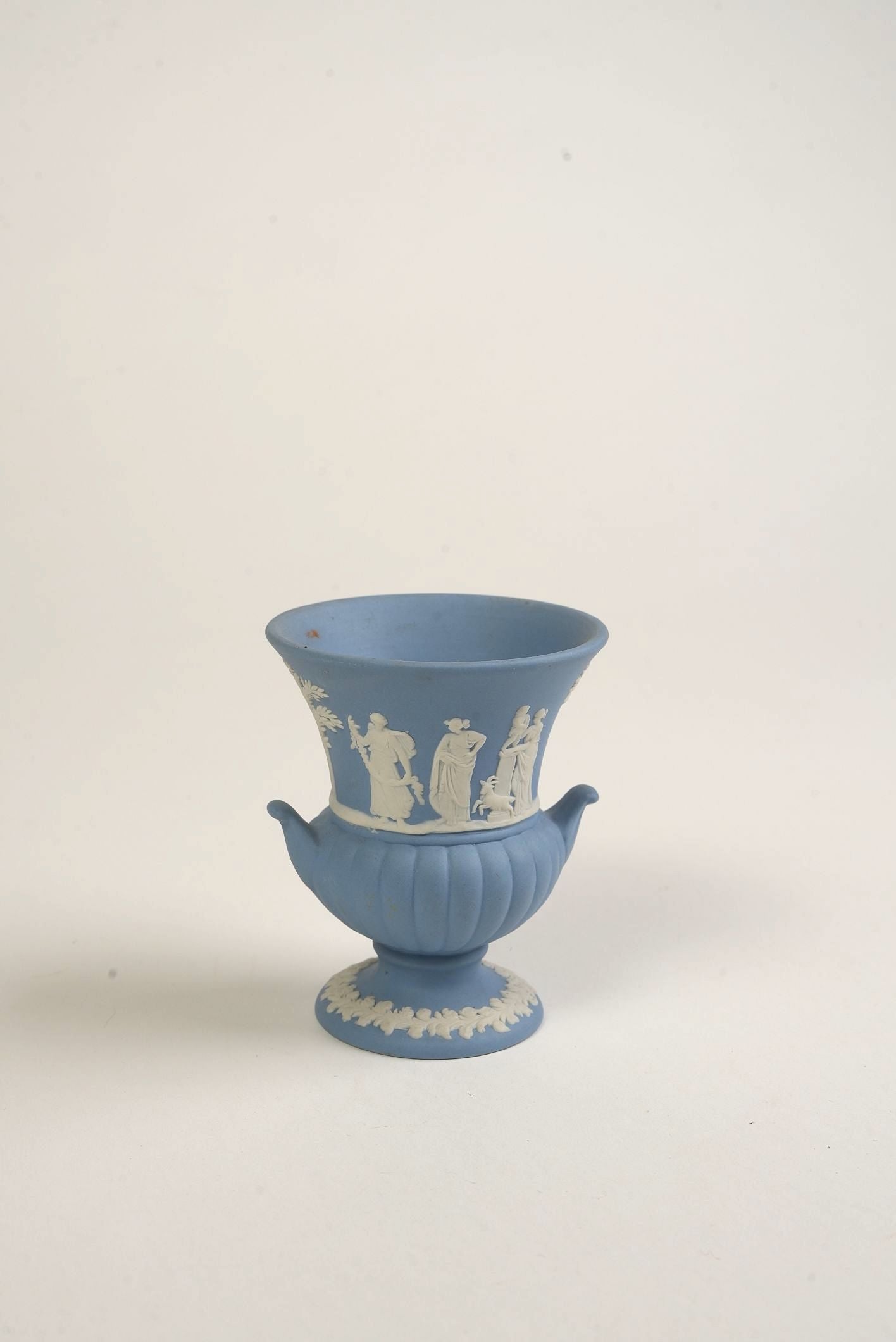 Blue ceramic Wedgwood urn with white relief design on a light gray background