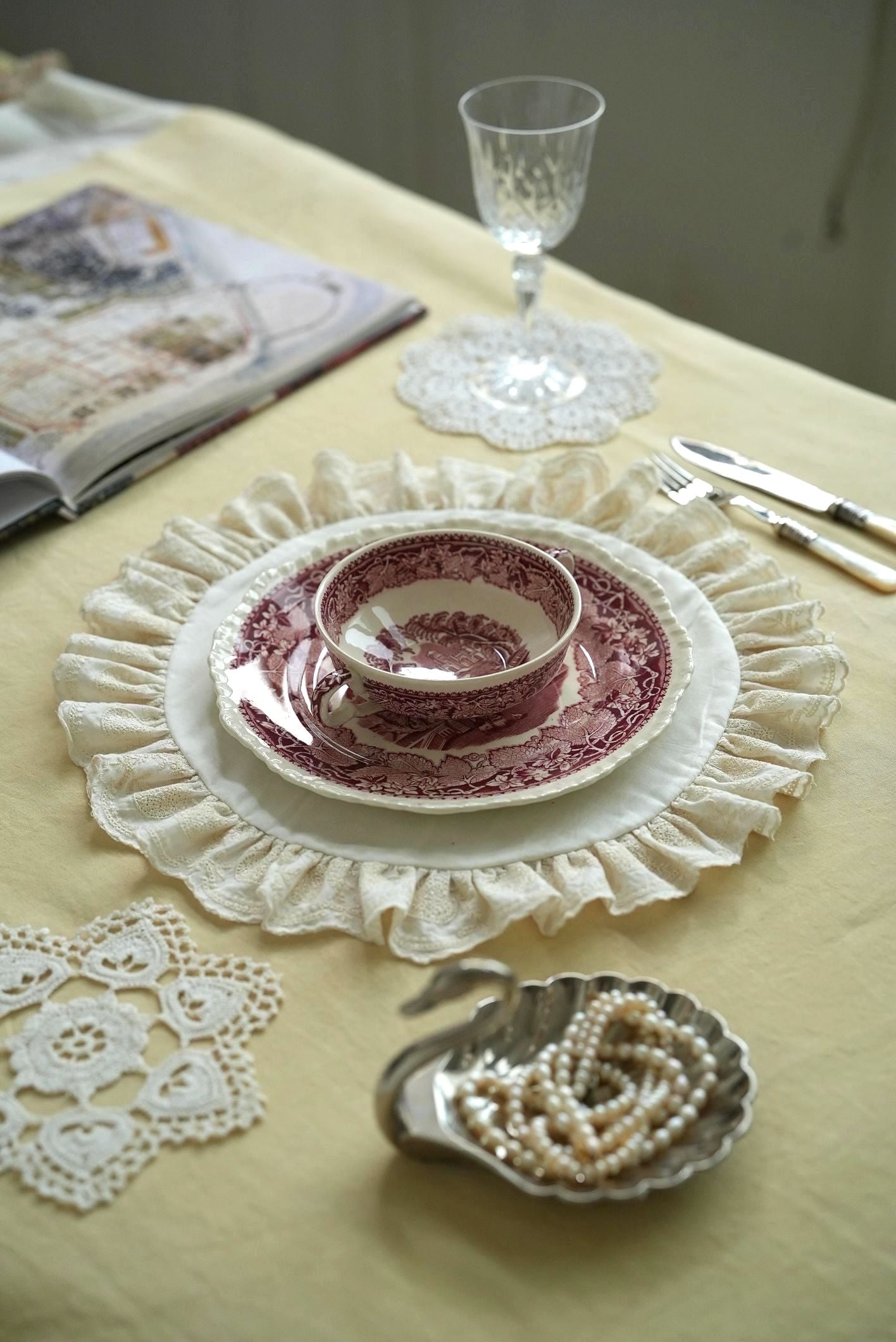 Vintage table setting with a teacup, saucer, and decorative plate on a yellow tablecloth.