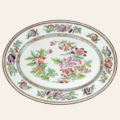 An oval ceramic platter with hand-painted floral patterns in vibrant colors, including green, pink, gold, and deep plum, with a decorative border. - Authentic antique piece 