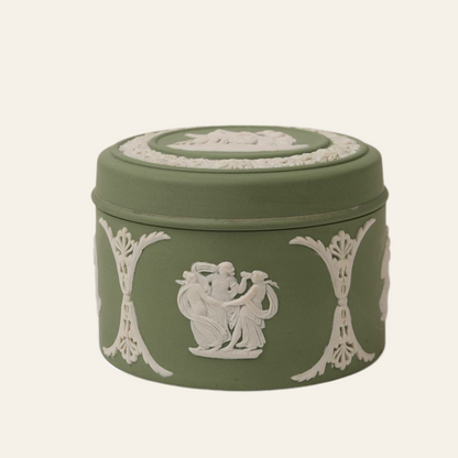 A round green Wedgwood ceramic trinket box with white relief decorations featuring neoclassical motifs.