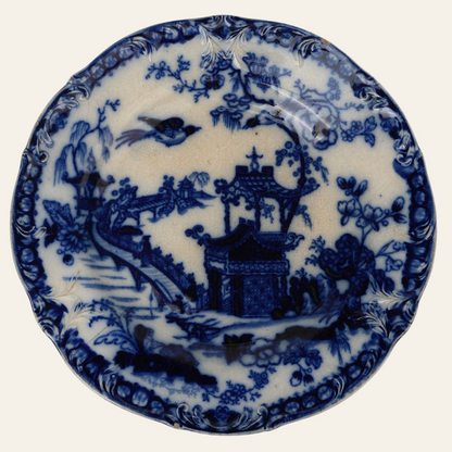 An antique Flow Blue ceramic plate with a Victorian Pagoda pattern featuring deep cobalt blue designs of pagodas, bridges, floral motifs, and birds on a creamy background.