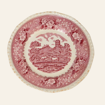 A medium-sized, red and white porcelain dinner plate with a pastoral scene featuring a horse and foal, trees, a village, and a tower, bordered with a floral pattern.
