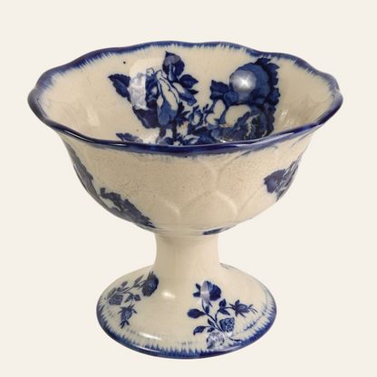 An antique Blakeney Ironstone pedestal centerpiece with a blue floral motif on a white background, featuring a fluted bowl and scalloped rim.