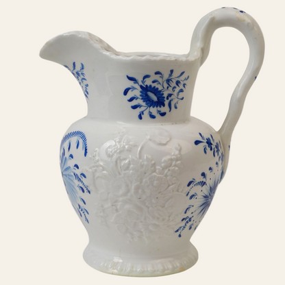 A vintage embossed ceramic jug with blue and white floral patterns, featuring a curved handle and a scalloped spout.