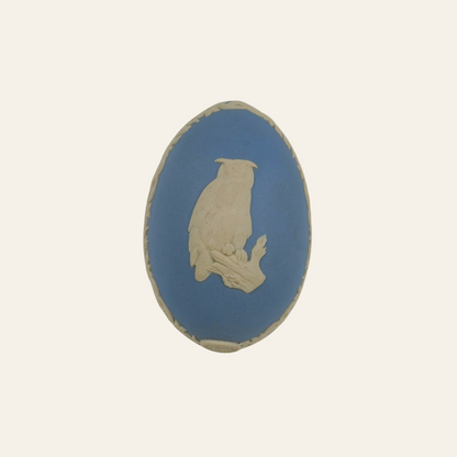 Oval-shaped blue and beige ceramic tile with a bird design on a white background