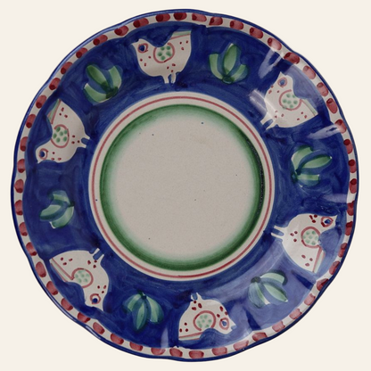 A vibrantly colored ceramic platter with a cobalt blue background, adorned with stylized bird motifs in white with green accents, and red details on the edge.