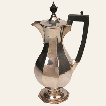 A vintage silver-plated coffee pot with a faceted body, a gracefully rounded base, a hexagonal pedestal, an angular black handle, a domed lid with a classic finial, and a curved spout.