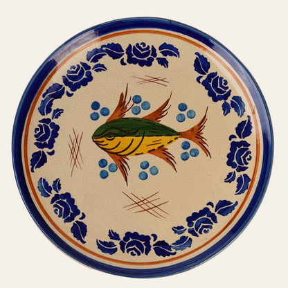 A ceramic plate with a hand-painted fish motif in the center, surrounded by a deep blue floral border.