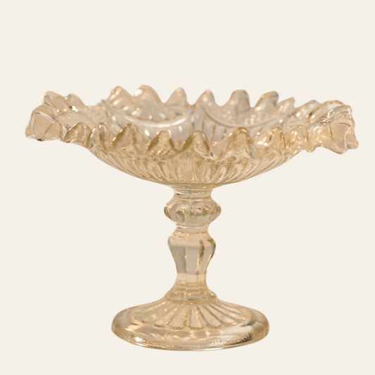 A vintage decorative crystal dish with a scalloped edge and a sturdy pedestal base, featuring an intricate geometric pattern.